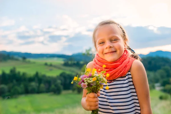 山の風景の背景の野生の花の花束を持つ少女の笑みを浮かべてください — ストック写真