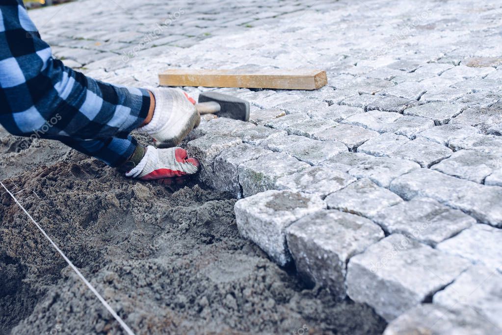 construction worker placing stone tiles for pavement, terrace. Worker placing granite cobblestone pavement at terrace