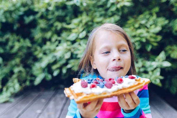 ワッフル 笑顔の庭にホイップ クリーム ラズベリー ブルーベリーの屋外でワッフルを食べる女子高生 — ストック写真