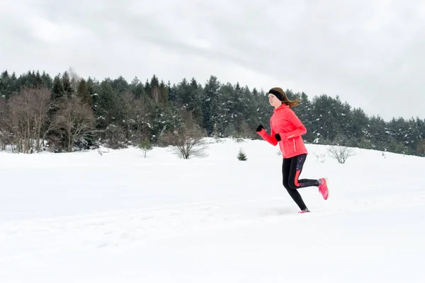 Молода жінка біжить на снігу в зимових горах в теплому одязі — стокове фото