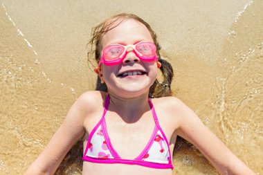 Küçük bir kız kumlu bir plaj üzerinde sırt üstü yatıyor