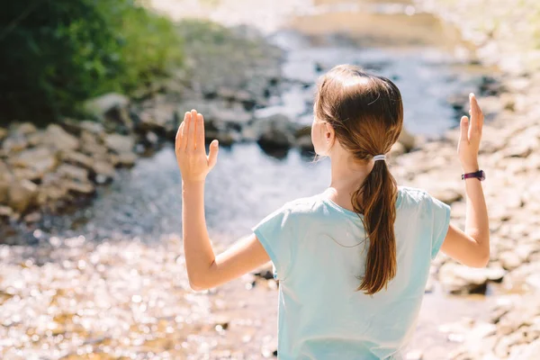 Young girl raises her arms praying on the banks of a mountain st — Stock Photo, Image