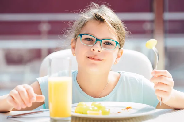 パンケーキ、新鮮なフルーツを食べてオレンジjを飲む陽気な女の子 — ストック写真