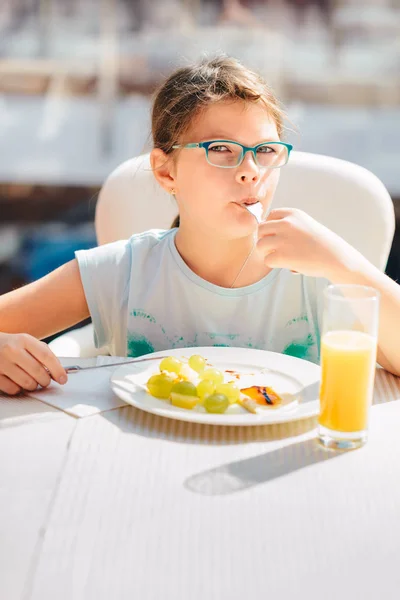 Fille gaie manger des crêpes, des fruits frais et de boire de l'orange — Photo