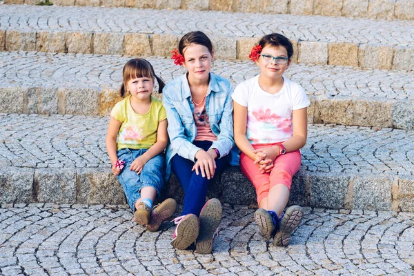 Three sisters sitting on stone stairs - during summer holidays — Stock Photo, Image