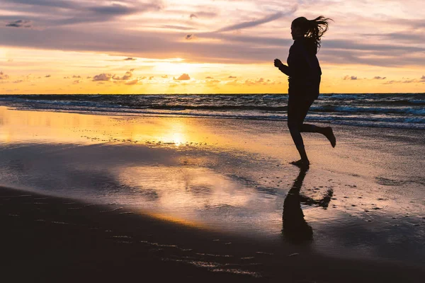 Adolescente correndo descalço em uma praia à beira-mar ao pôr do sol — Fotografia de Stock