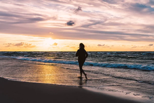 Teenage girl running barefoot on a sandy seaside beach at sunset — Stock Photo, Image