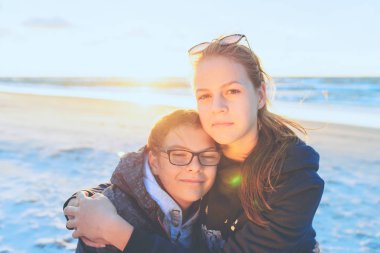 Gün batımında deniz sahilinde birbirlerine sarılan iki kız kardeş