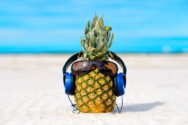 Kumsalda güneş gözlüğü ve kulaklık ile Ananas
