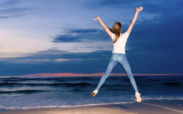 Tiener meisje springen op het strand in de schemering tijd — Stockfoto