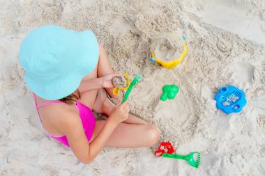 Mutlu çocuk yazın kumsalda kumla oynuyor.