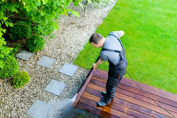 power washing - man cleaning terrace with a power washer - high water pressure cleaner on wooden terrace surface