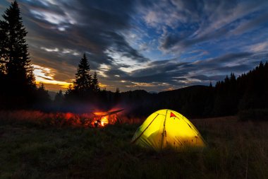 Ukrayna Karpatları 'nda akşam. Günbatımının arka planında çimlerde parlayan çadırlar. Dağlarda kamp yapmak..