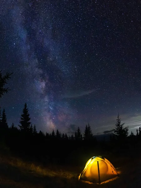 Perseid meteor shower and the Milky Way in the Carpathian Mountains. Evening on a hike. tent glows on a background of night starry sky.