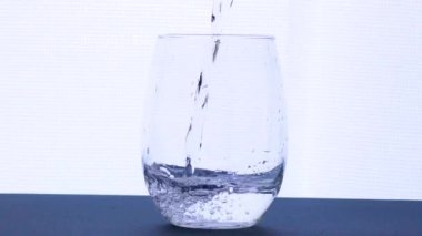 Temiz suyu bardağa damlatıyor. Parlak arka planda izole edilmiş. Su yaşam konseptidir