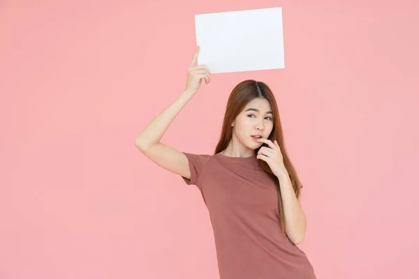 Joven asiática sonriente mujer sosteniendo cartel publicitario y señalando el dedo. Retrato aislado sobre fondo rosa con espacio para copiar —  Fotos de Stock