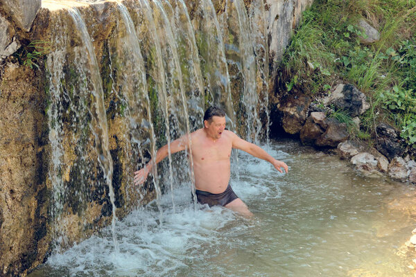 man bathes in a mountain stream falls on the stones in nature