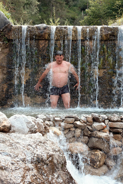 man bathes in a mountain stream falls on the stones in nature