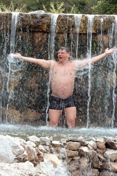 man bathes in a mountain stream falls on the stones in nature