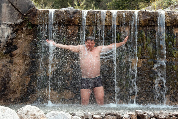 man bathes in a mountain stream falls on the stones in nature