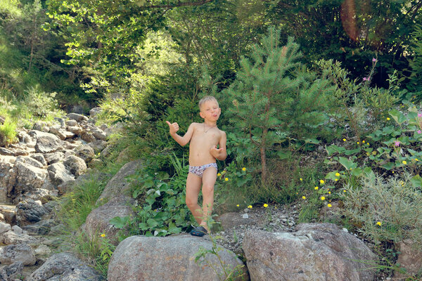 the child sits by the brook on the rocks in nature
