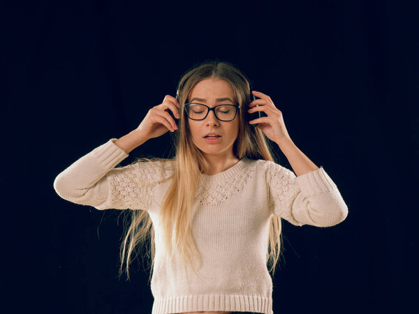 Beautiful enjoying young woman listening the music in wireless headphone on dark black background