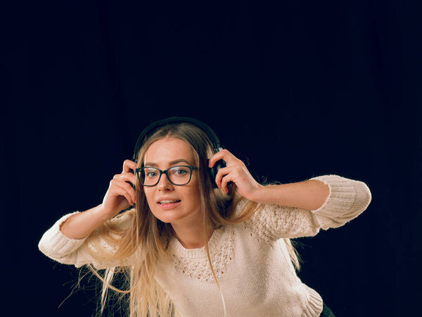 Beautiful enjoying young woman listening the music in wireless headphone on dark black background