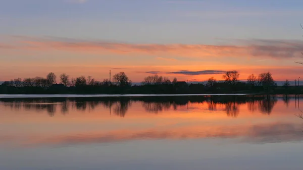 Röd solnedgång över vattnet i en sjö och by — Stockfoto