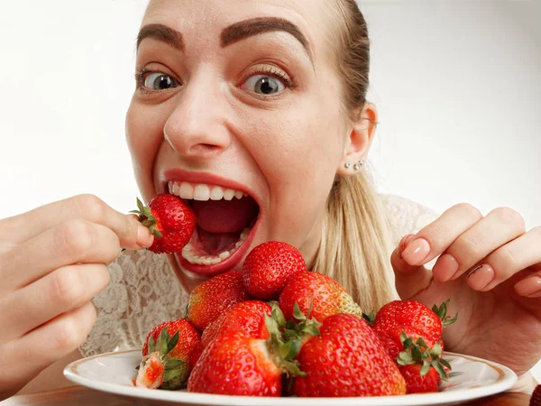Girl eagerly eating strawberries on white background. — Stock Photo, Image