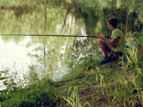 Adolescente niño atrapa una caña de pescar en el estanque . — Foto de Stock