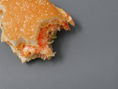 gri bir arka plan üzerinde pirlet peynir ve domates ile ısırılan büyük burger