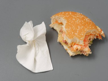 gri bir arka plan üzerinde pirlet peynir ve domates ile ısırılan büyük burger