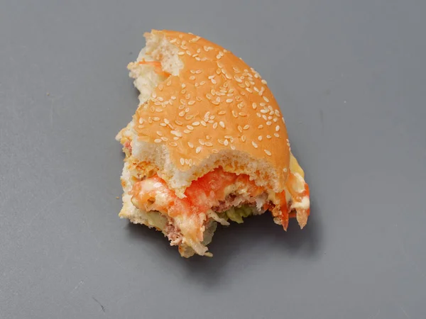 bitten big burger with cutlet cheese and tomato on a gray background