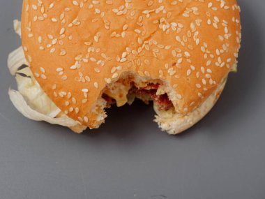 gri bir arka plan üzerinde pirlet peynir ve domates ile ısırılan büyük burger
