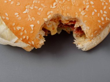gri bir arka plan üzerinde pirlet peynir ve domates ile ısırılan büyük burger