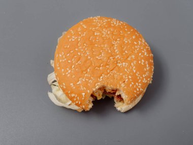 gri bir arka plan üzerinde pirlet peynir ve domates ile ısırılan büyük burger