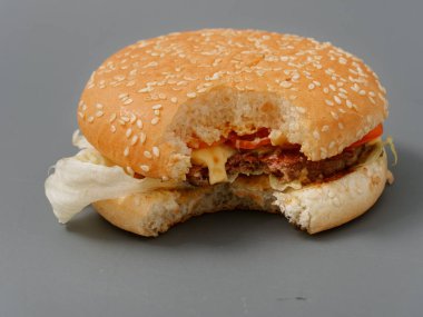 gri bir arka plan üzerinde pirlet peynir ve domates ile ısırılan büyük burger