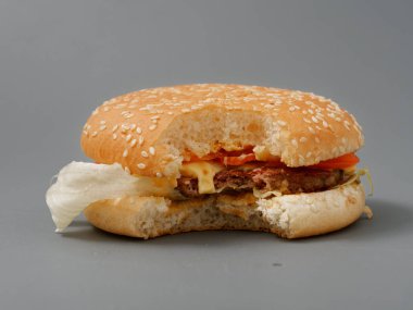 gri bir arka plan üzerinde pirlet peynir ve domates ile ısırılan büyük burger