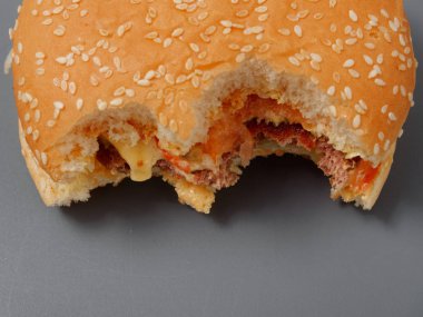gri bir arka plan üzerinde pirlet peynir ve domates ile ısırılan büyük burger