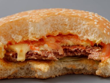 gri bir arka plan üzerinde pirlet peynir ve domates ile ısırılan büyük burger