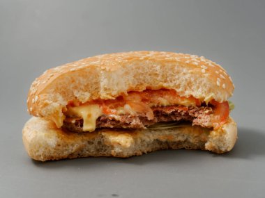 gri bir arka plan üzerinde pirlet peynir ve domates ile ısırılan büyük burger