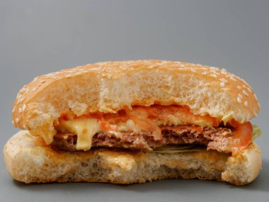 gri bir arka plan üzerinde pirlet peynir ve domates ile ısırılan büyük burger