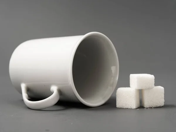 Verfijnde suiker knobbel witte en witte beker op een grijze achtergrond — Stockfoto
