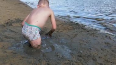 Çocuk kumsalda kumla oynuyor.