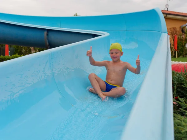 Menino monta passeios de corrediça de água no parque aquático — Fotografia de Stock