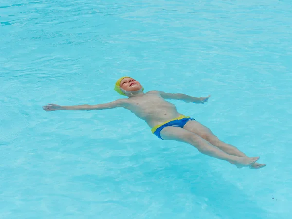 Niño nada en una piscina con agua azul — Foto de Stock