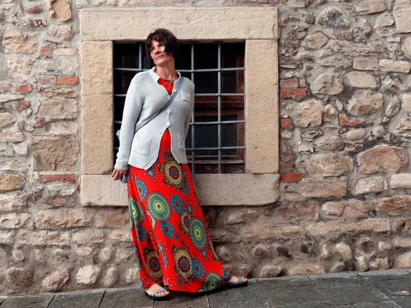 Krásná žena v červených šatech stojí na kamenné stěně starého města — Stock fotografie