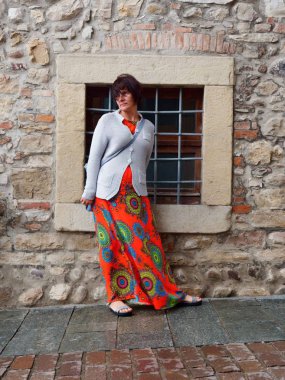 kırmızı elbiseli güzel kadın eski şehrin taş duvarında duruyor