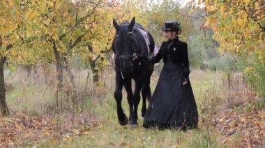 Siyah elbiseli atlı kadın siyah bir ata önderlik ediyor.