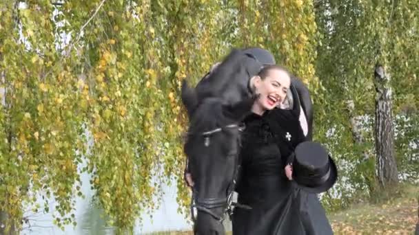 Chica en un vestido negro con un caballo negro de cerca — Vídeos de Stock